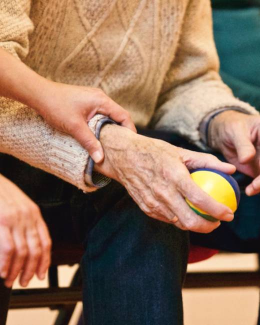 An elderly person receives support from a caregiver, holding hands indoors, showcasing compassion.