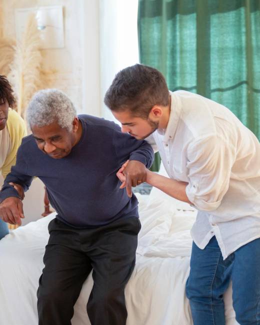 An elderly man receiving assistance from caregivers in a cozy home environment.